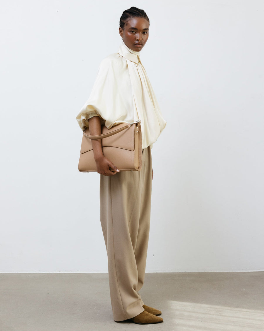 Woman holding a beige handbag against a plain background