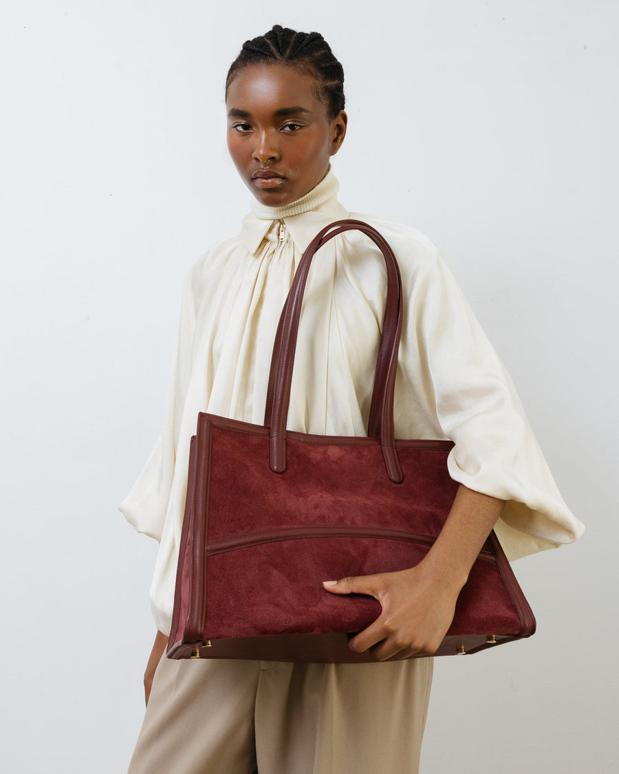 Person holding a maroon handbag against a plain background