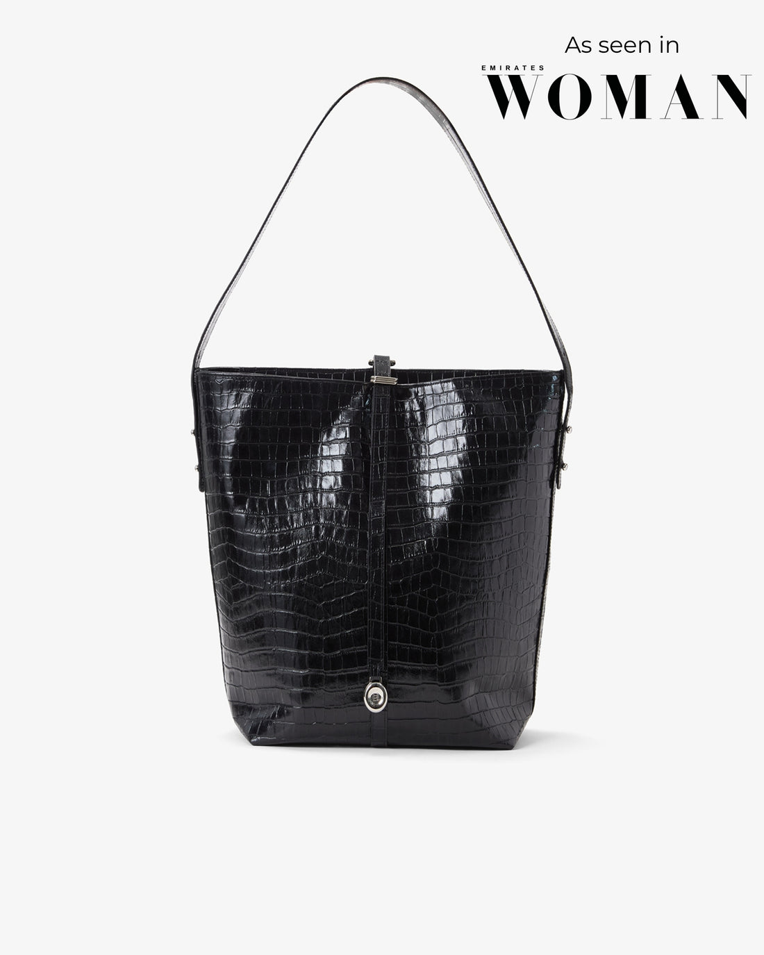 A black crocodile-embossed leather shoulder bag with a single strap, shown against a light gray background with 'As seen in Emirates WOMAN' text in the upper right.