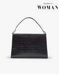 A black crocodile-embossed leather handbag with a single top handle and silver-tone hardware, shown against a light gray background with 'As seen in WOMAN' text in the upper right.