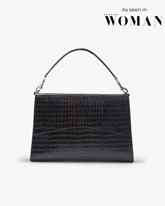 A black crocodile-embossed leather handbag with a single top handle and silver-tone hardware, shown against a light gray background with 'As seen in WOMAN' text in the upper right.