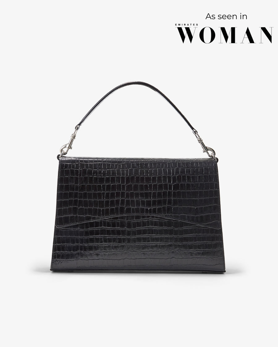 A black crocodile-embossed leather handbag with a single top handle and silver-tone hardware, shown against a light gray background with 'As seen in WOMAN' text in the upper right.