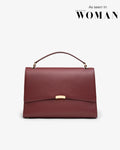 A structured top-handle handbag in burgundy textured leather with a gold-tone clasp and hardware, shown against a light gray background with 'As seen in EMIRATES WOMAN' text in the top right corner.