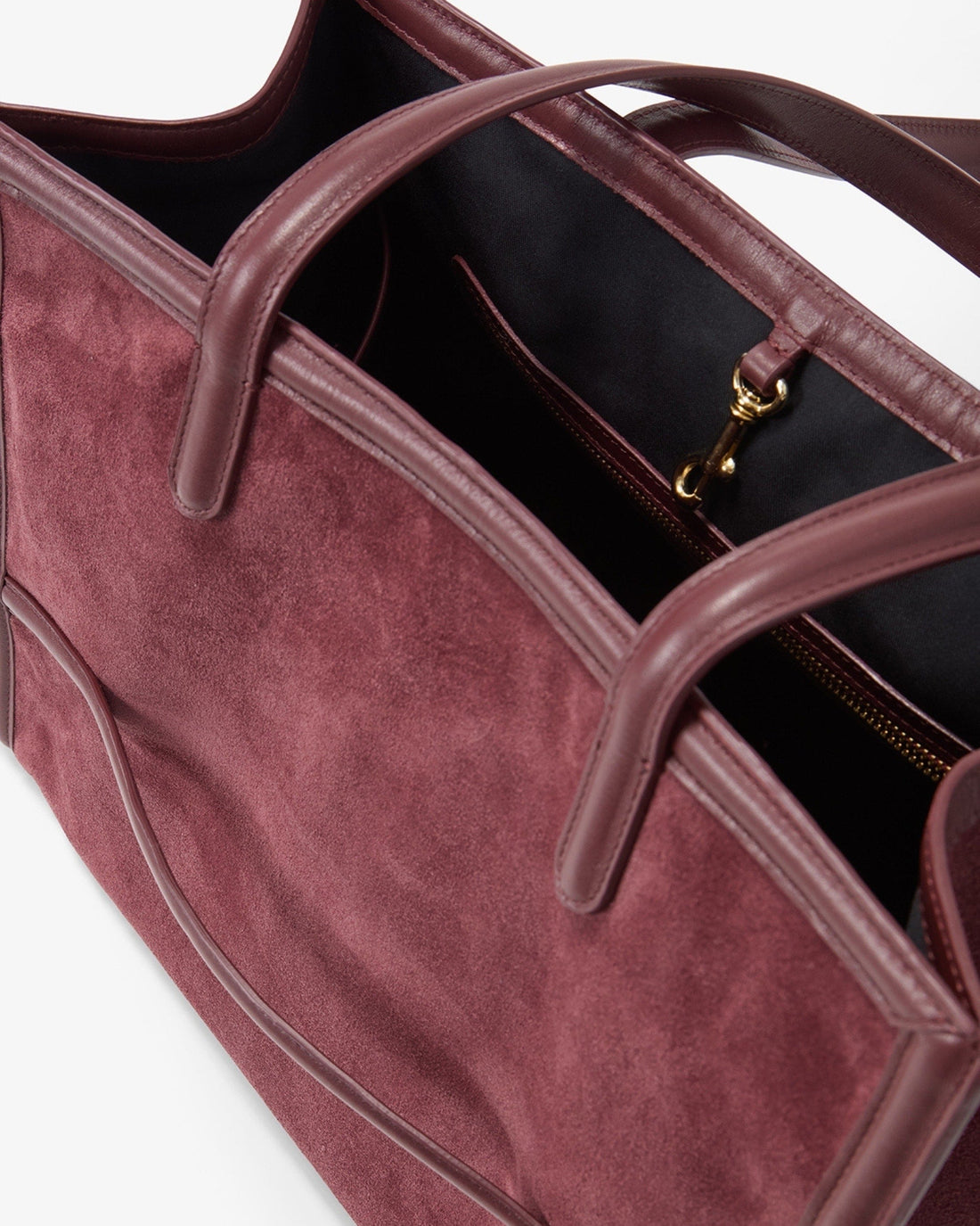 Close-up of a burgundy suede tote bag with dark  leather trim and handles, showing a black interior and gold zipper pull.