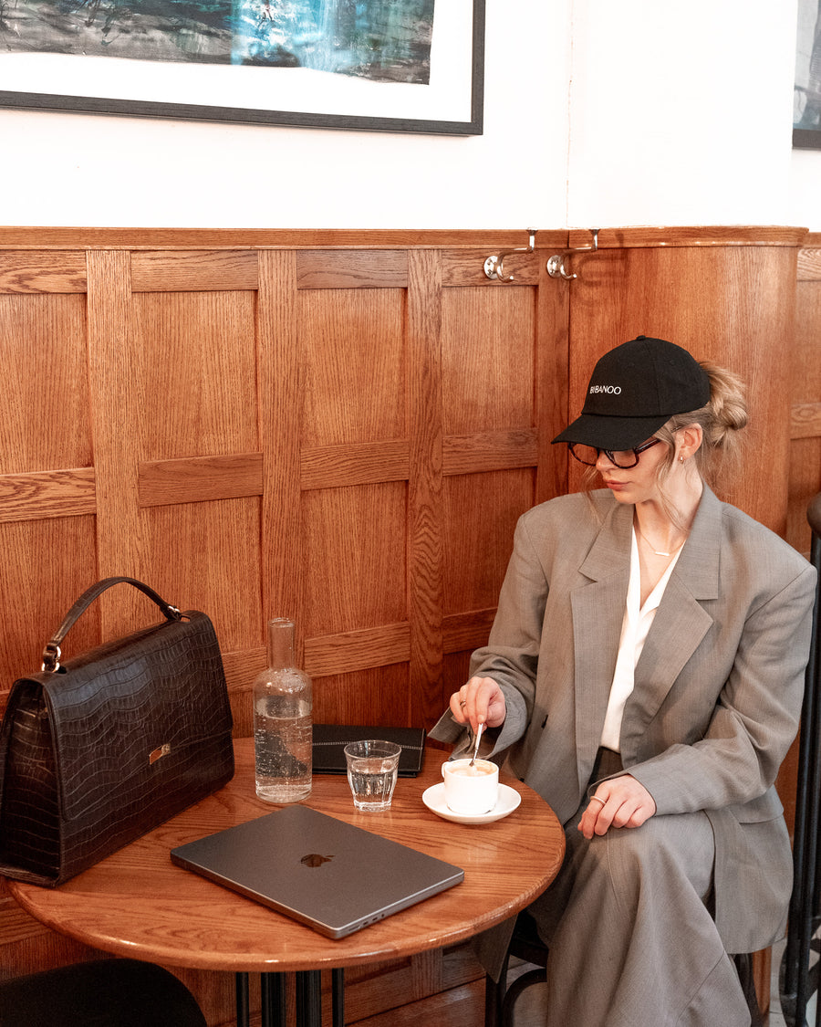 Woman sitting at a wooden table in a cafe, eating from a bowl with a fork.
