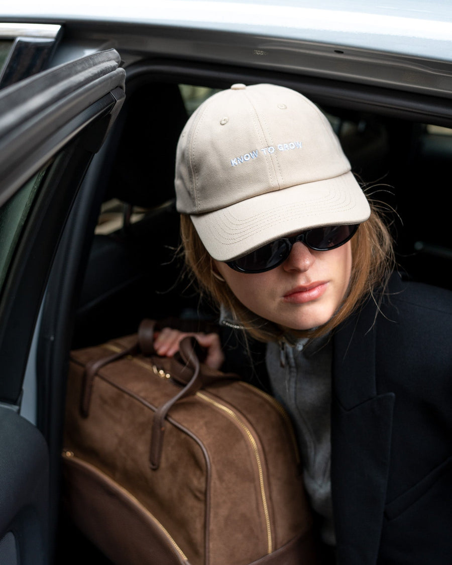 Person getting into a car with a brown leather bag, wearing a beige cap and sunglasses.