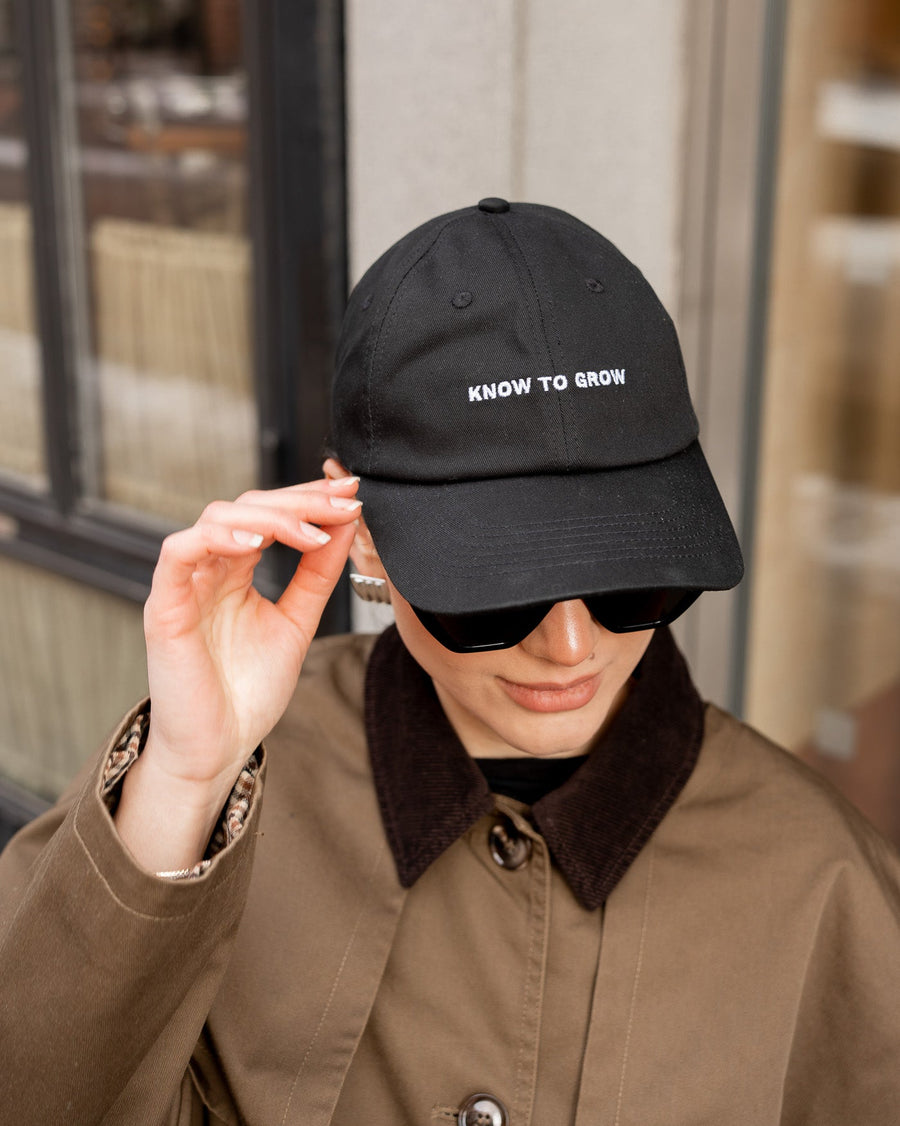 Person wearing a black cap with 'KNOW TO SLOW' text, standing indoors.