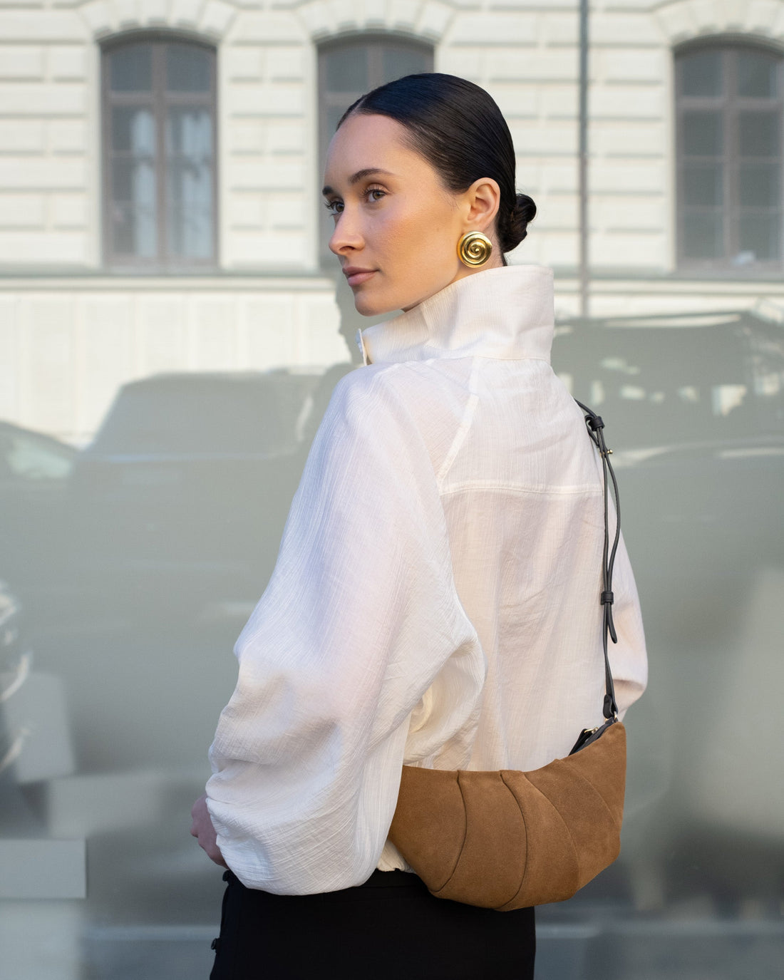 Woman wearing a brown suede bag with a black cross body strap and metal hardware