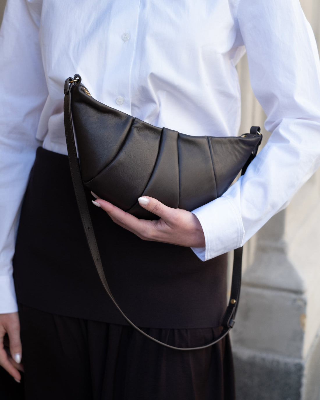 Woman holding a dark brown leather hand bag with gold hardware and a cross body strap