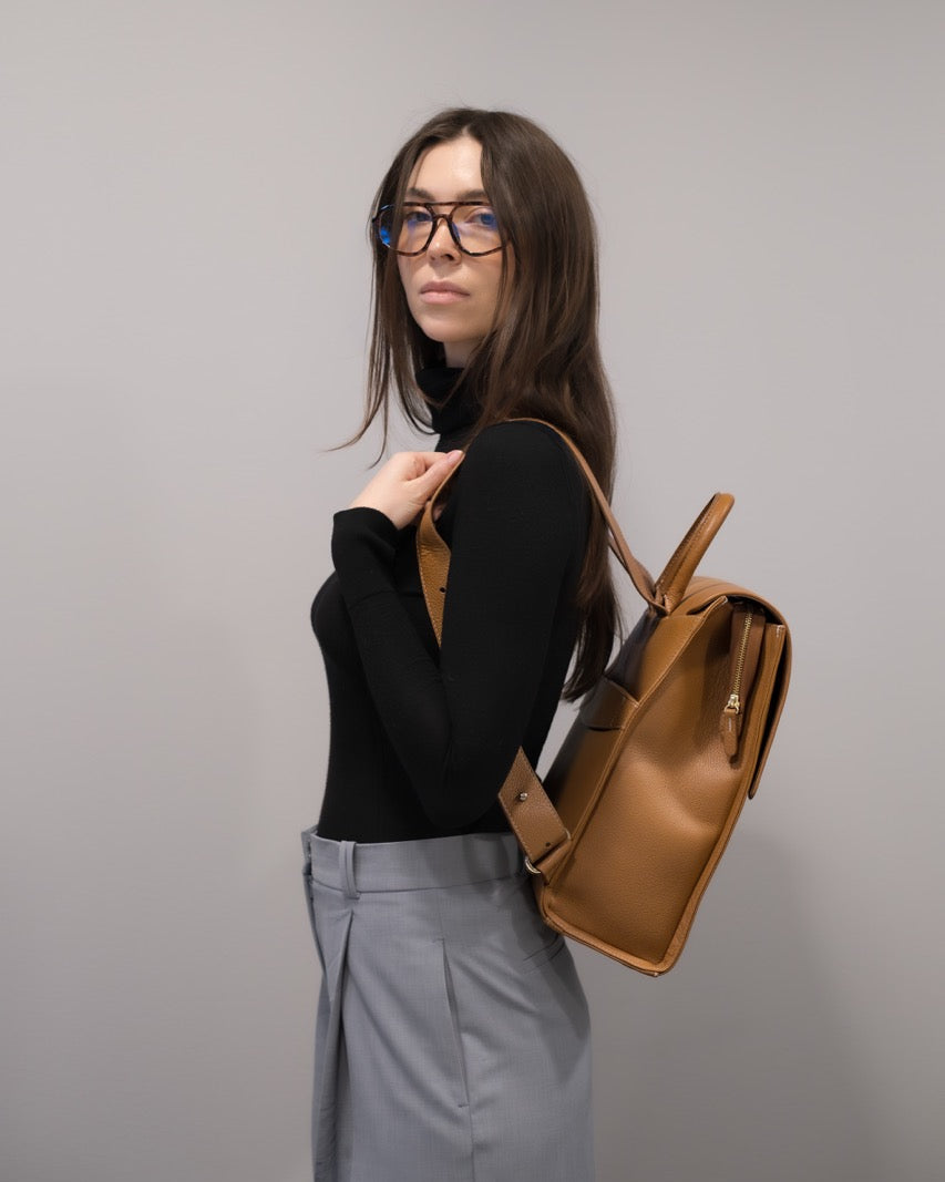 A tan leather backpack with a top handle, shown from the front against a plain white background.
