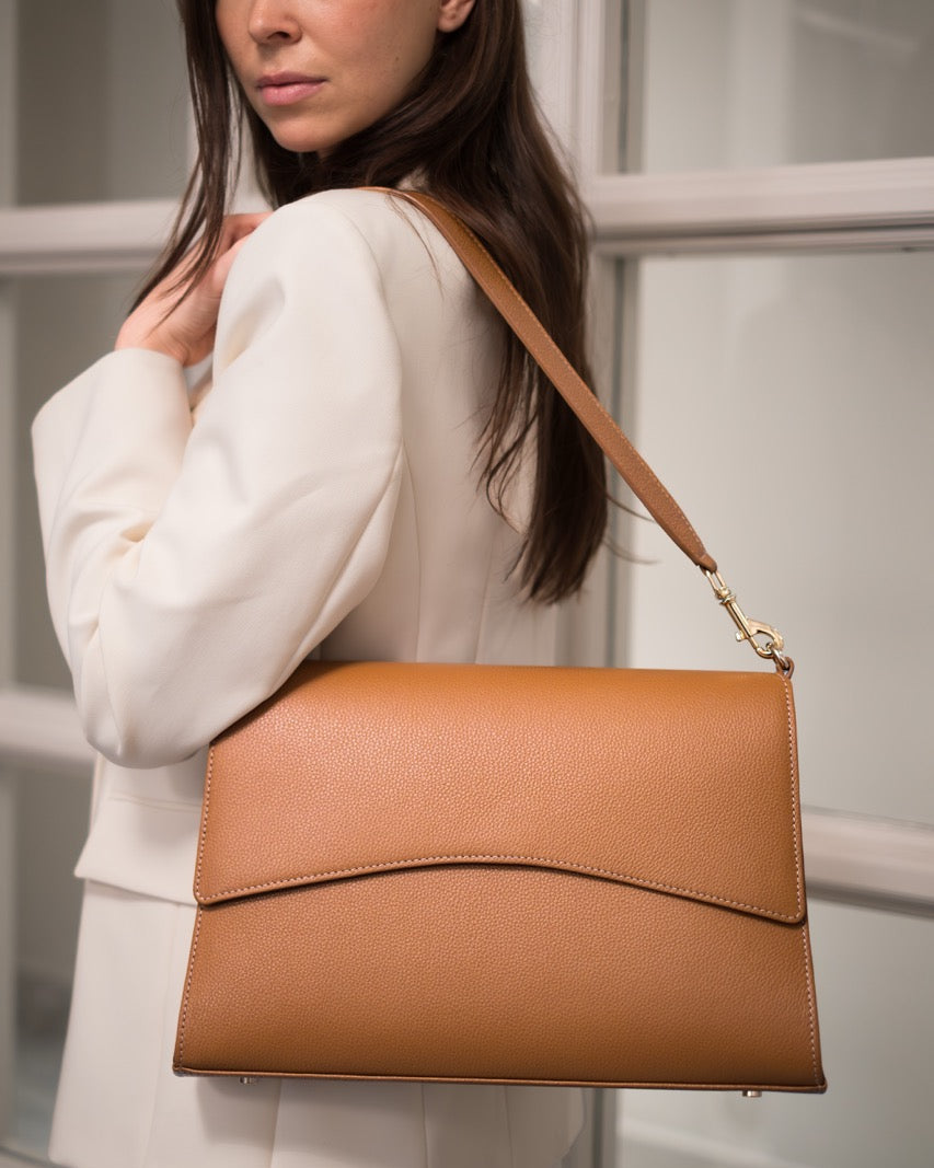 A tan leather shoulder bag with a top handle and gold-tone hardware, shown against a plain white background.