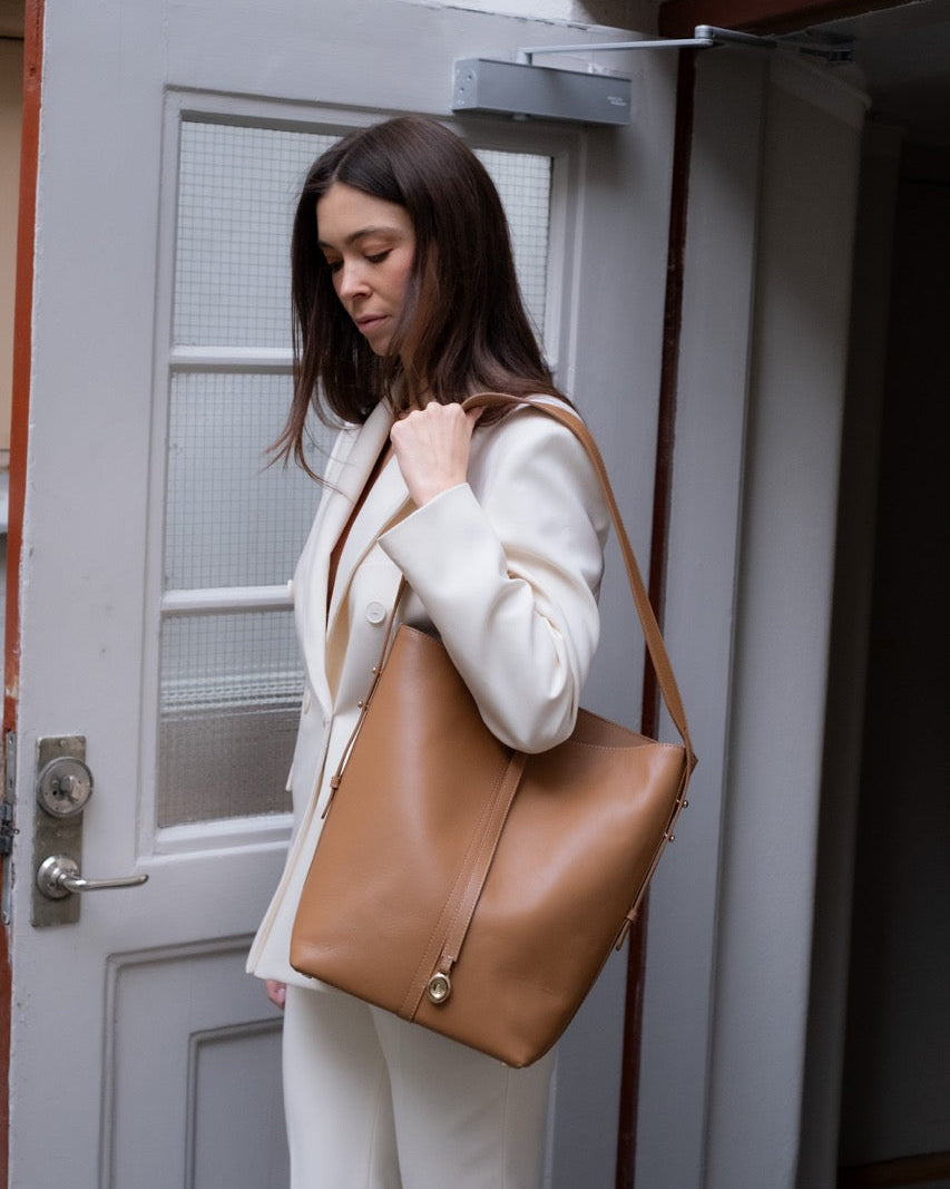 Woman holding a brown leather bag in front of a door