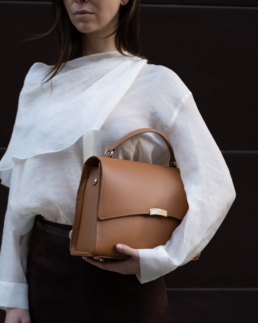Woman holding a tan leather handbag with gold hardware
