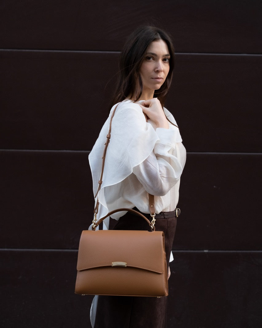 Woman wearing a tan leather bag with gold hardware