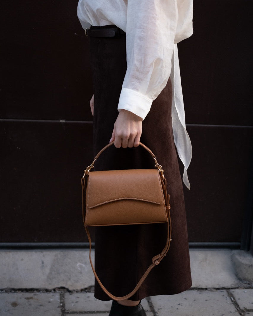 Person holding a brown leather handbag against a dark background