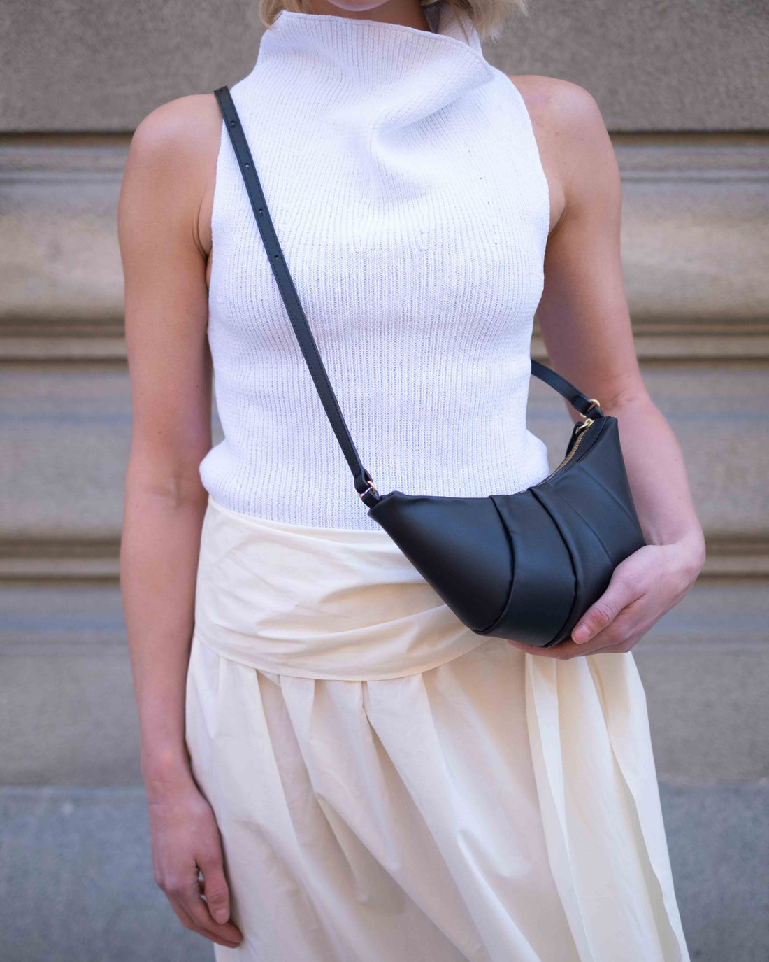 Woman wearing a white outfit and a black leather crossbody bag with a pleated surface.