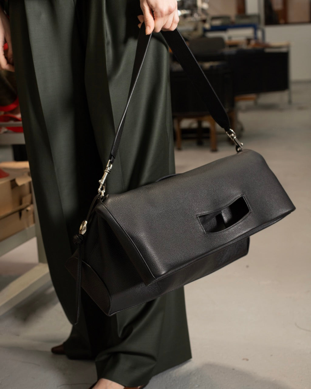 A woman wearing a black folded leather tote bag in a shoulder strap. 