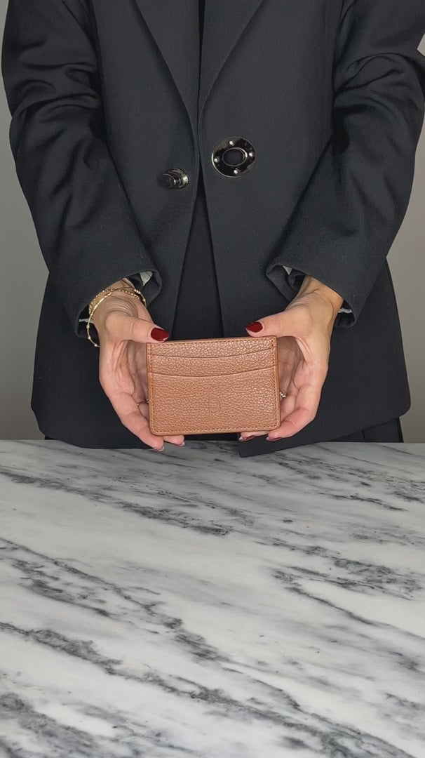 A woman holder a tan leather card holder with an embossed "B" logo, inserting cards into it. 