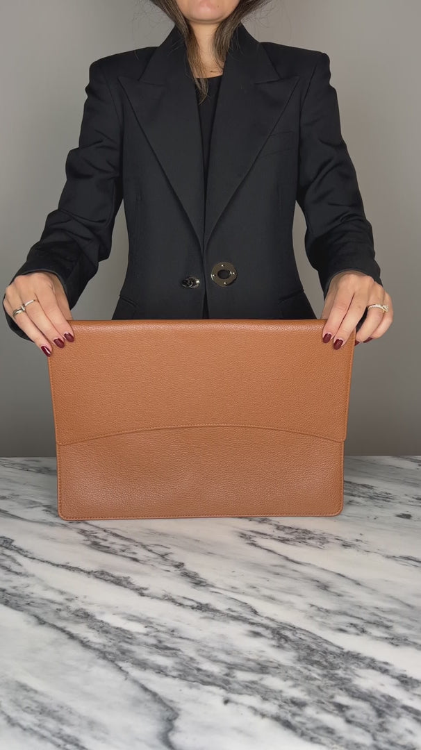 A woman demonstrating a tan laptop cover, inserting a laptop into it on a marble table. 