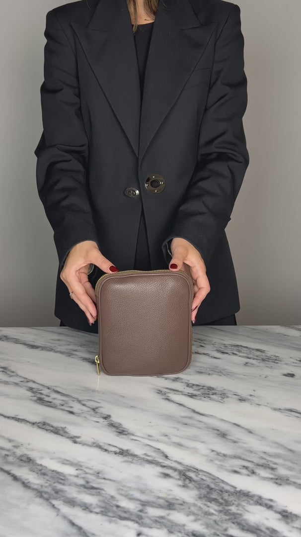 Packing a dark brown leather cable organizer with cords, in mesh pockets. The organizer closes with a metal zipper. 