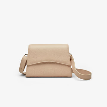 A beige grained leather handbag with light gold metalware and an adjustable strap for a comfortable crossbody or shoulder fit. 